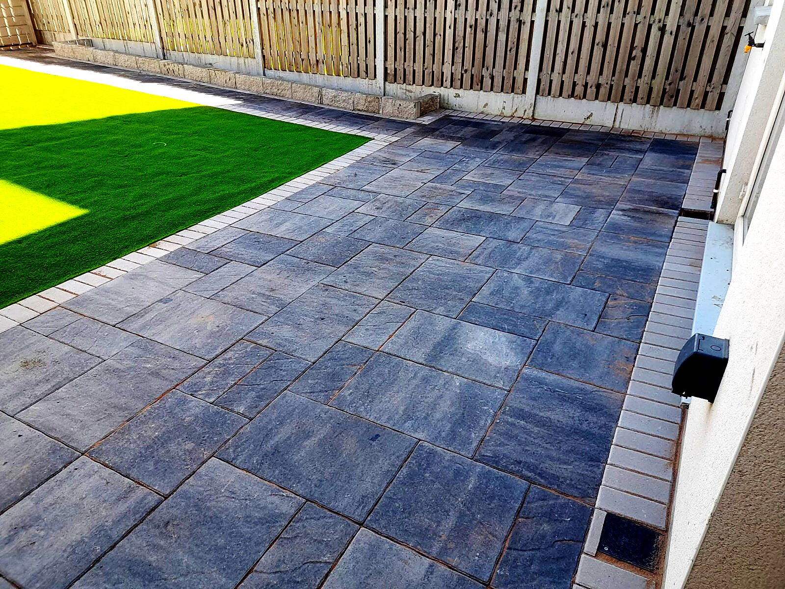 Side view of large-format grey paving meeting artificial grass