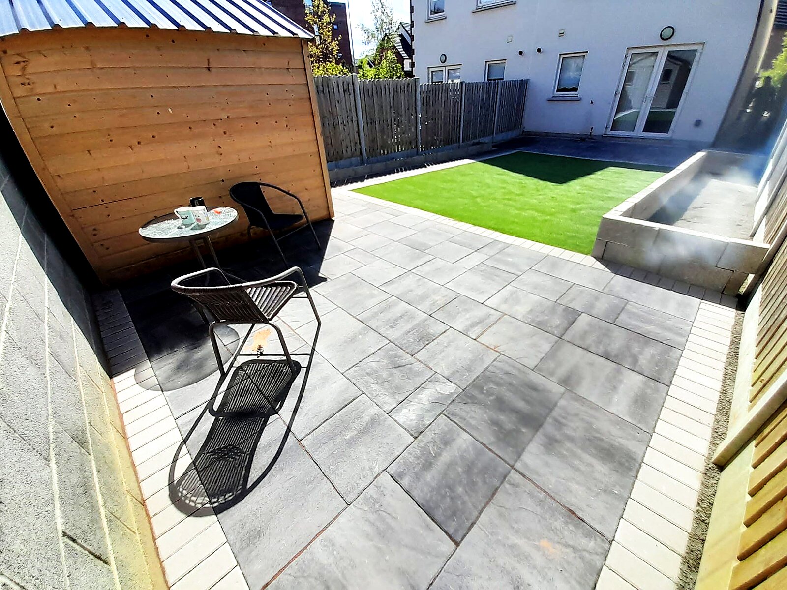 Finished patio seating area beside a timber shed with artificial grass beyond